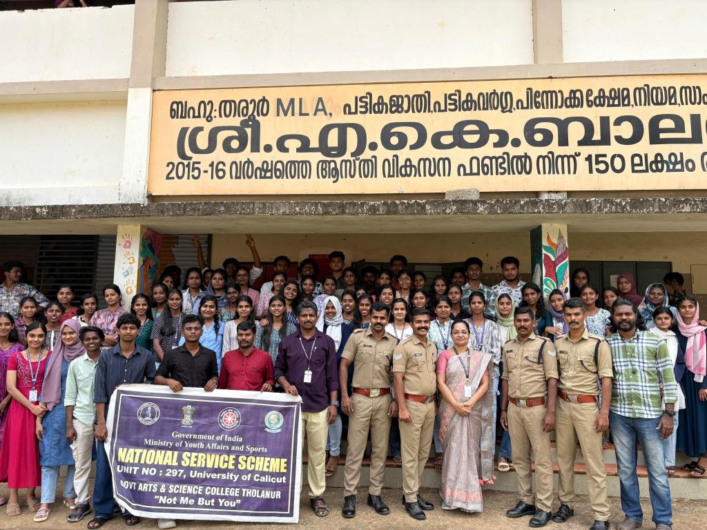 A large group of students and faculty members posing in front of a building, with a banner for the National Service Scheme visible, indicating their participation in a community service program.